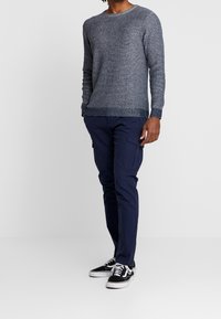 Donkergrijze gebreide trui met een geribde ronde hals, gecombineerd met marineblauwe cargobroek en zwarte sneakers met witte veters en zolen.