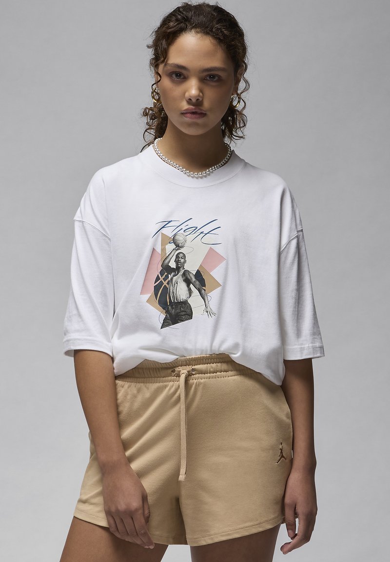 T-shirt bianca oversize con stampa grafica di un giocatore di basket, abbinata a pantaloni corti beige con coulisse e logo.