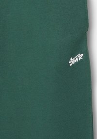 Hanorac de culoare verde închis, realizat dintr-un material moale, cu un logo mic brodat de culoare albă poziționat în partea dreaptă jos.