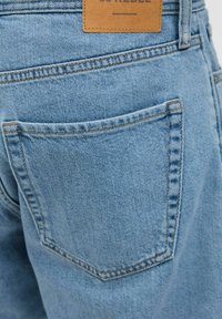 Gros plan sur la poche arrière d'un jean en denim bleu avec une étiquette de marque en cuir marron cousue au-dessus de la poche.