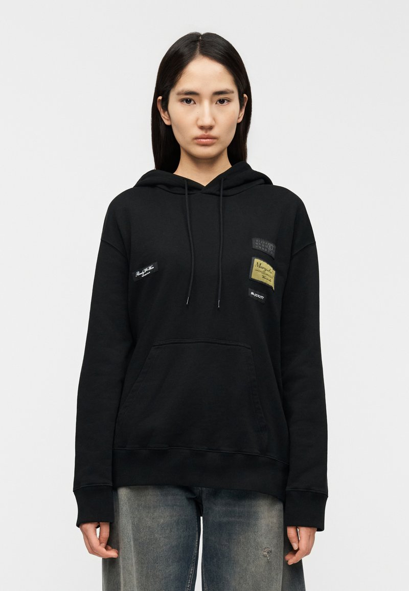 Black hoodie with a kangaroo pocket, drawstrings, and multiple fabric patches in different shapes and colors. Cotton blend material.