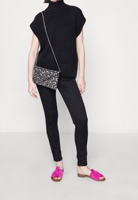 Black knitted oversized sweater with a ribbed hem, black fitted pants, and pink suede slide sandals with a knotted detail. Black and white patterned bag.