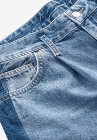 Sinised denim püksid, millel on vöökoht, esipocket ja nähtav õmblus. Kanga tekstuur on veidi kulunud ja kergelt pestud efekti tekitav.