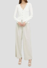 Vit stickad kavaj med V-ringning, långa ärmar och knappframsidan. Matchas med ljusbeiga vida byxor och vita sandaler.