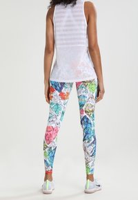 Leggings feature a vibrant diamond pattern in multiple colors on a white background, paired with a sheer white tank top.