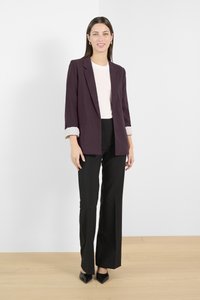 Blazer color bordeaux con maniche arrotolate, abbinato a un top bianco aderente e pantaloni neri a gamba larga. Presenta un design su misura e una texture liscia.