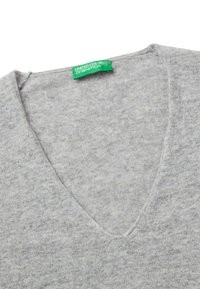 Šedý svetr s výstřihem do V vyrobený z měkké tkaniny. Disponuje čistým, minimalistickým designem se zelenou etiketou s nápisem „United Colors of Benetton.“