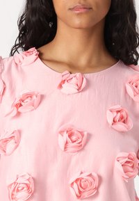 Top rosa a maniche corte con applicazioni floreali testurizzate. Presenta un collo rotondo e un tessuto morbido e leggero.
