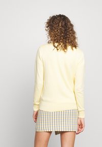 Jasnożółty sweter wykonany z miękkiego materiału, z okrągłym dekoltem i prążkowanymi mankietami, w zestawie z spódnicą w kratę.