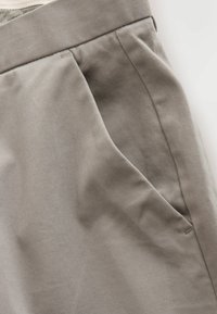 Khaki cotton trousers with a smooth texture, featuring a side pocket and subtle pleating at the waist. Minimalistic design.