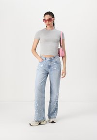 Camiseta ajustada de color gris claro, jeans de pierna ancha de color azul claro con efecto desgastado y bordes deshilachados, zapatillas beige, bolso rosa y gafas de sol rosas de gran tamaño.