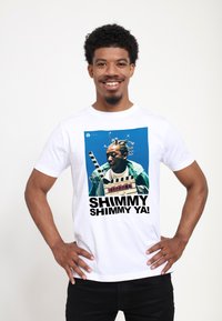 Hvid t-shirt med et farverigt grafikprint af en mand med fletninger, der holder et filmklapperbræt, med teksten "SHIMMY SHIMMY YA!" nedenfor.
