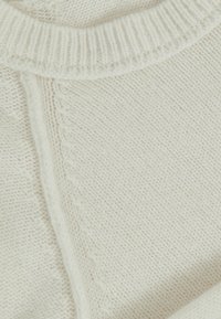 Gestrickter cremfarbener Pulloverstoff mit strukturiertem Muster, ausgestattet mit einem ribbelten Rundhalsausschnitt und einem Nahtdetail entlang der Seite.