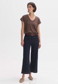 Top a scacchi marrone con scollo a V, jeans a gamba larga in denim scuro, cintura marrone e scarpe slip-on beige. Design semplice con vestibilità rilassata.