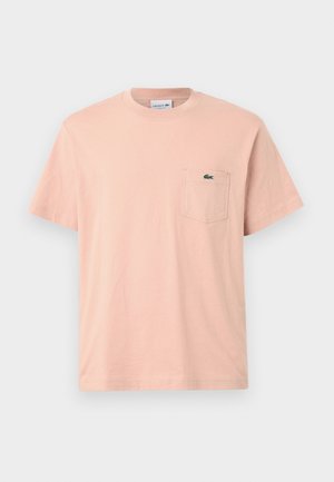 Pale pink cotton t-shirt with a round neckline, short sleeves, and a left chest pocket featuring a green Lacoste logo.