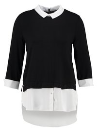 Svart långärmad topp med vit skjortkrage och manschetter, med en lagerdesign där ett vitt skjortslut kikar fram längst ner.