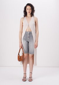 Beige ribbed knit sleeveless top with front tie detail, paired with grey denim shorts and a brown handbag. Black strappy sandals complete the look.