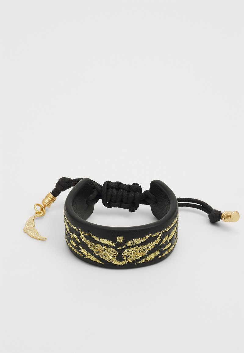 Bracelet noir réglable avec motif d'aile brodé en or et breloque en forme d'aile dorée sur la fermeture à cordon.