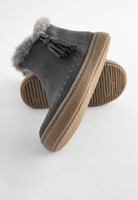 Stivali ankle in suede grigio con accenti in pelliccia, frange decorative e suole in gomma texturizzata. Cuciture visibili lungo il bordo superiore.