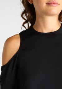 Svart kall-axel topp med en slät textur, rund halsringning och korta ärmar, med en design som visar axlarna.