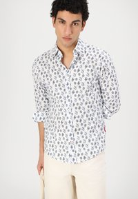 Hvit knapp-up skjorte med et marineblått mønster av blekksprut og intrikate design. Stoffet har en glatt tekstur med oppbrettede ermer.