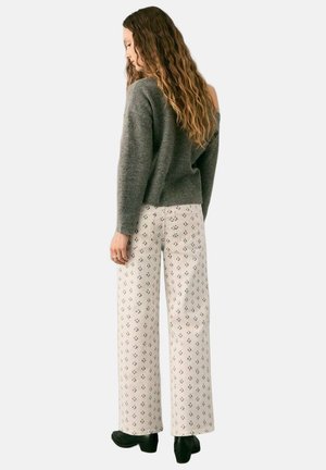 Suéter gris de punto con diseño de hombros descubiertos, combinado con pantalones anchos color crema que presentan un sutil patrón floral. Calzado negro.