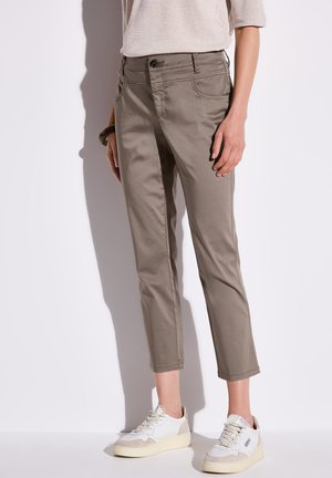 Pantalons en coton de couleur kaki, longueur cheville, avec un devant plat, un design à cinq poches et une fermeture par bouton. Portés avec des baskets blanches.