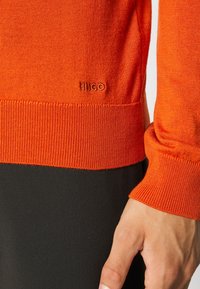 Pomarańczowy, długi sweter z dzianiny z długimi rękawami, z prążkowymi mankietami i obrębem. Logo "HUGO" wyszyte w tym samym kolorze na dolnej przedniej części.