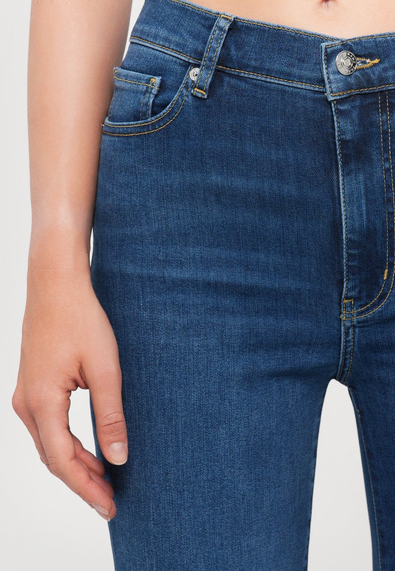 Donkerblauwe denim jeans met een hoge taille, vijf-pocket ontwerp, contrasterende gouden stiksels en een zilveren knoopsluiting.