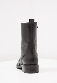 Stivale alla caviglia in pelle nera con punta arrotondata, perforazioni decorative lungo le cuciture e un tacco basso. Presenta un inserto sul retro per la trazione e una finitura liscia.