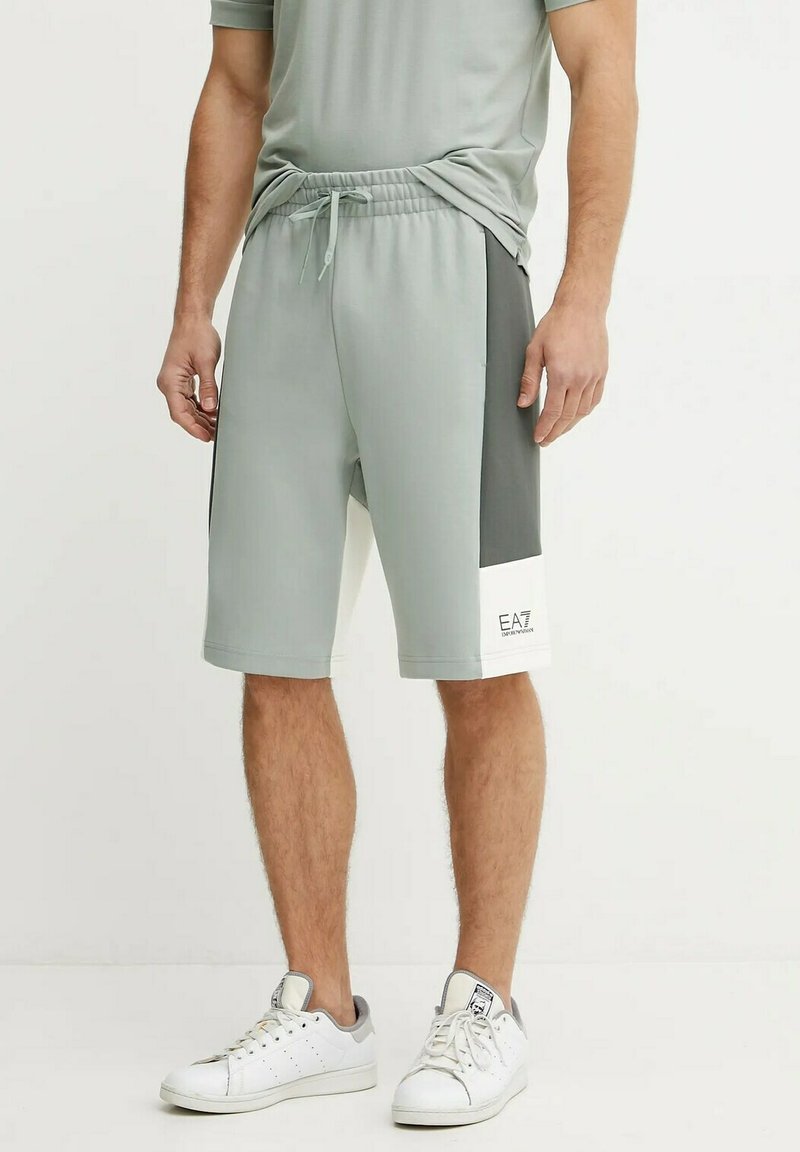 Pantaloni sportivi di colore verde chiaro con pannelli laterali grigio scuro, vita elastica e un accento bianco con logo nell'angolo inferiore.