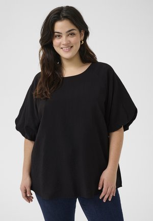 Blouse noire légère avec un col rond et des manches courtes bouffantes. Texture lisse et coupe ample, associée à un jean en denim foncé.