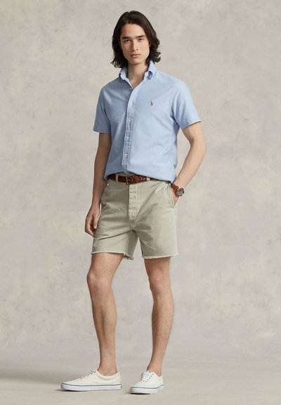 Camisa azul-clara de botões com mangas curtas, calções bege, cinto castanho e ténis brancos. Design simples, material algodão, visual casual.