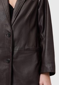 Blazer in pelle marrone con una superficie liscia, rever a punta e due bottoni. Include tasche laterali e spalle strutturate.