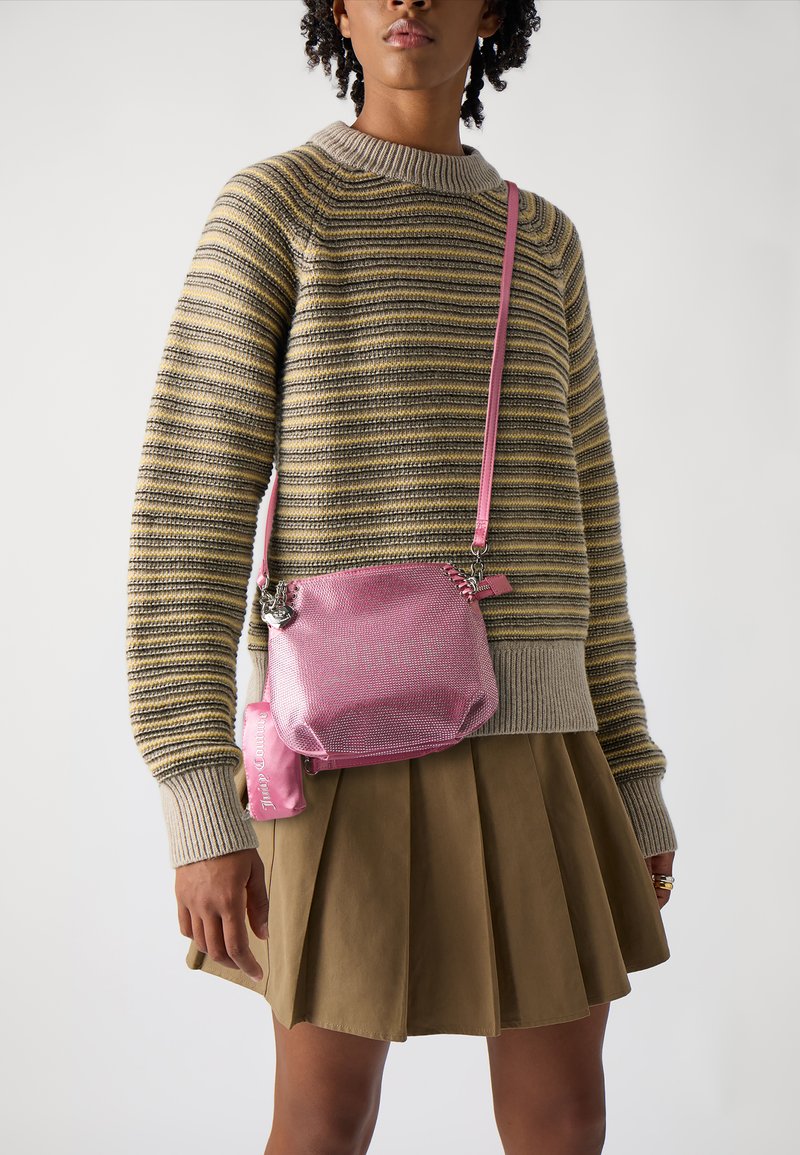Sac en bandoulière en métal rose avec une surface texturée, des accents en argent et une fermeture éclair. Porté avec un pull rayé et une jupe.