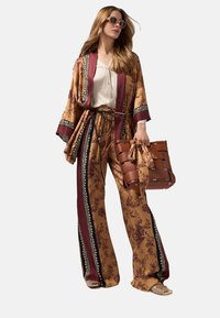 Vloeiende, gemêleerde kimono in goud en bordeaux met een strikceintuur. Gecombineerd met een wijd pijpmodel broek, een wit shirt en een geweven bruine handtas.