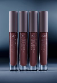 Fire flydende læbeprodukter med bløde matte mauve nuancer i klare tuber, med uigennemsigtige mauve låg og enkle hvide tekstetiketter.