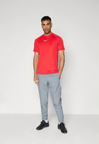 Piros sportpóló rövid ujjakkal és kerek nyakkivágással, világosszürke melegítőnadrággal, fekete oldalsávokkal. Fekete sportcipő.