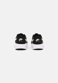Mustat ja valkoiset urheilukengät, joissa on verkkokangas- ja synteettinen päällinen, pehmustettu pohja ja näkyvä Nike-logo kantapäässä.