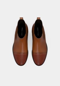 Brown leather shoes with a contrasting darker toe, featuring perforated detailing and a smooth upper. Slip-on design with pull tabs.