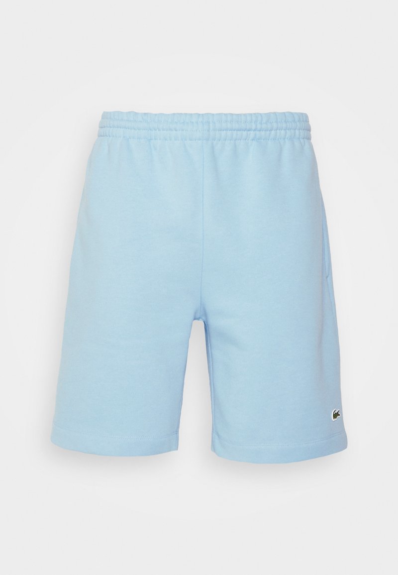 Shorts en coton bleu clair avec une ceinture élastique, des poches latérales et un petit logo vert en bas à droite. Texture lisse.