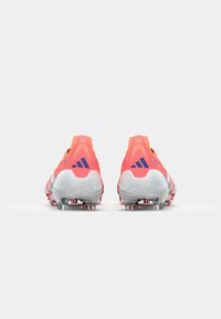 Scarpette da football di un brillante colore rosa con suole grigie, caratterizzate da una superficie liscia, un tacco prominente e un logo a tre strisce in blu navy.
