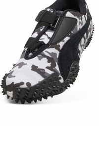 Zwart-witte camouflage sportshoe met een getextureerd oppervlak, voorzien van klittenband straps, een gewatteerde kraag en een rubberen buitenzool met spikes.