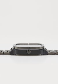 Montre carrée noire avec un boîtier en métal mat, bracelet en maillons métalliques gris, et couronne visible sur le côté. Design épuré et minimaliste.