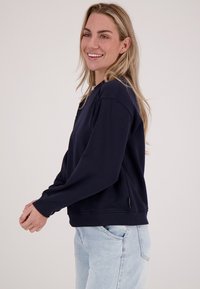Marineblauwe sweatshirt met lange mouwen, geribbelde manchetten en zoom. Gemaakt van zachte stof. Bevat een discrete logotag aan de linkerkant.