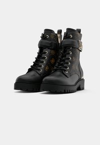 Bottines noires avec un dessus en cuir verni et en tissu à motifs. Comprend des accessoires en or, un laçage à l'avant, une fermeture éclair sur le côté et une semelle robuste.
