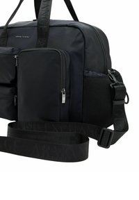 Borsone in nylon nero con molteplici tasche con zip, accenti testurizzati, tracolla con logo e una combinazione di texture liscia e in rete.