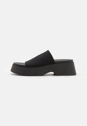 Sort platform-sandaler med tyk sål og bredt stofrem over foden, sidevisning på en ensartet lys baggrund.