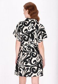 Korte mouw jurk van beige stof met gedurfde zwarte spiralen en patronen, met een getailleerde taille en een relaxte pasvorm, ideaal voor casual dragen.