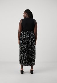 Black sleeveless top with a relaxed fit paired with wide-leg trousers featuring a white abstract leaf pattern. Heeled sandals complete the look.